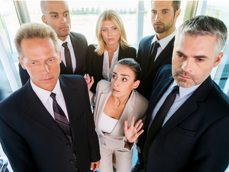 Une femme d'affaires coincée dans un ascenseur avec d'autres hommes et femmes d'affaires.